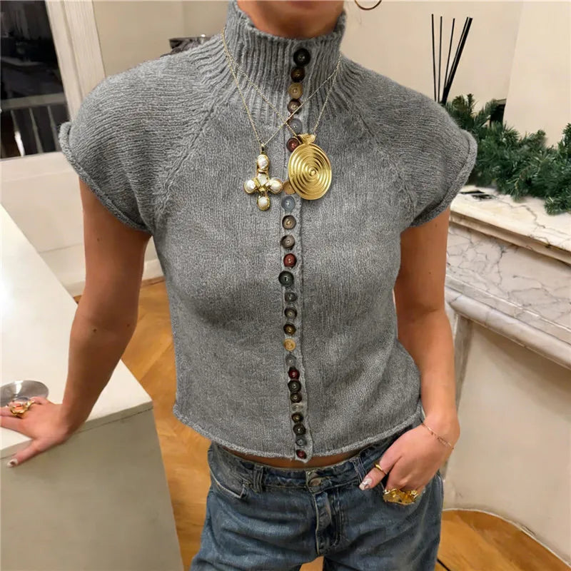 Person wearing a gray sleeveless top with decorative buttons and gold necklace indoors.
