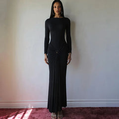 Woman wearing a black dress standing against a plain wall.