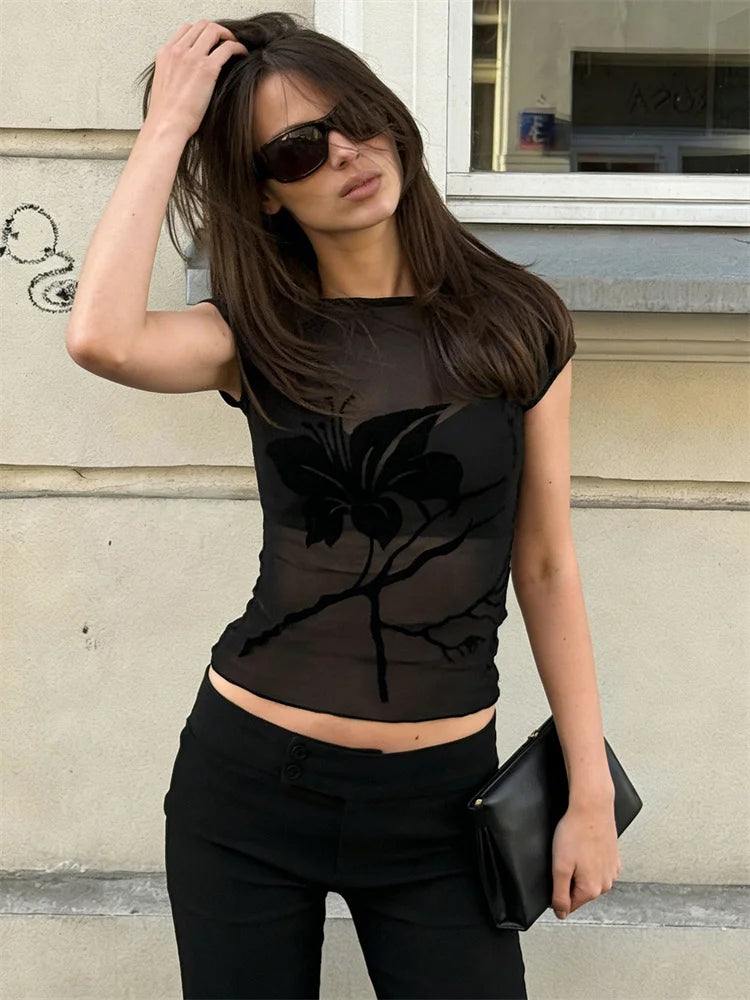 Woman wearing a black sheer top with a floral design outdoors.