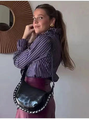 Woman wearing a striped shirt and carrying a black bag with silver studs against a neutral wall.