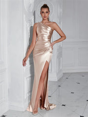 Woman wearing a beige one-shoulder evening gown with a high slit in a elegant interior setting.