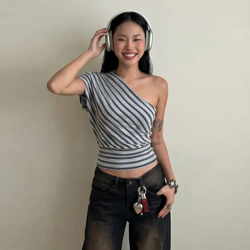 Woman wearing a striped one-shoulder top and headphones, standing against a plain background