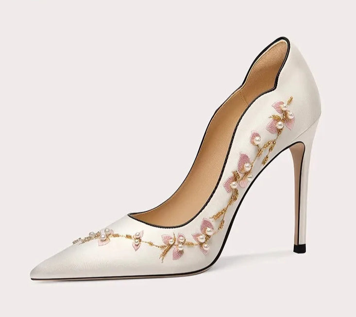 White high-heeled shoe with floral embroidery on a light gray background