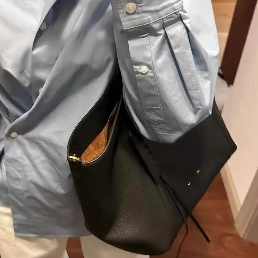 Person wearing a light blue shirt with a black leather bag over their shoulder.