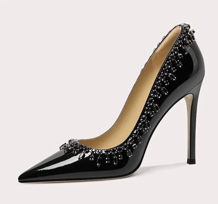 Black high-heeled shoe with decorative embellishments on a light gray background