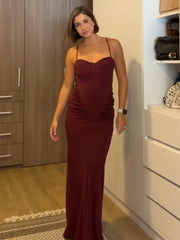 Woman wearing a burgundy evening gown in a room with wooden cabinets and white drawers.