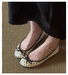 Close-up of a person wearing white polka dot ballet flats with black trim