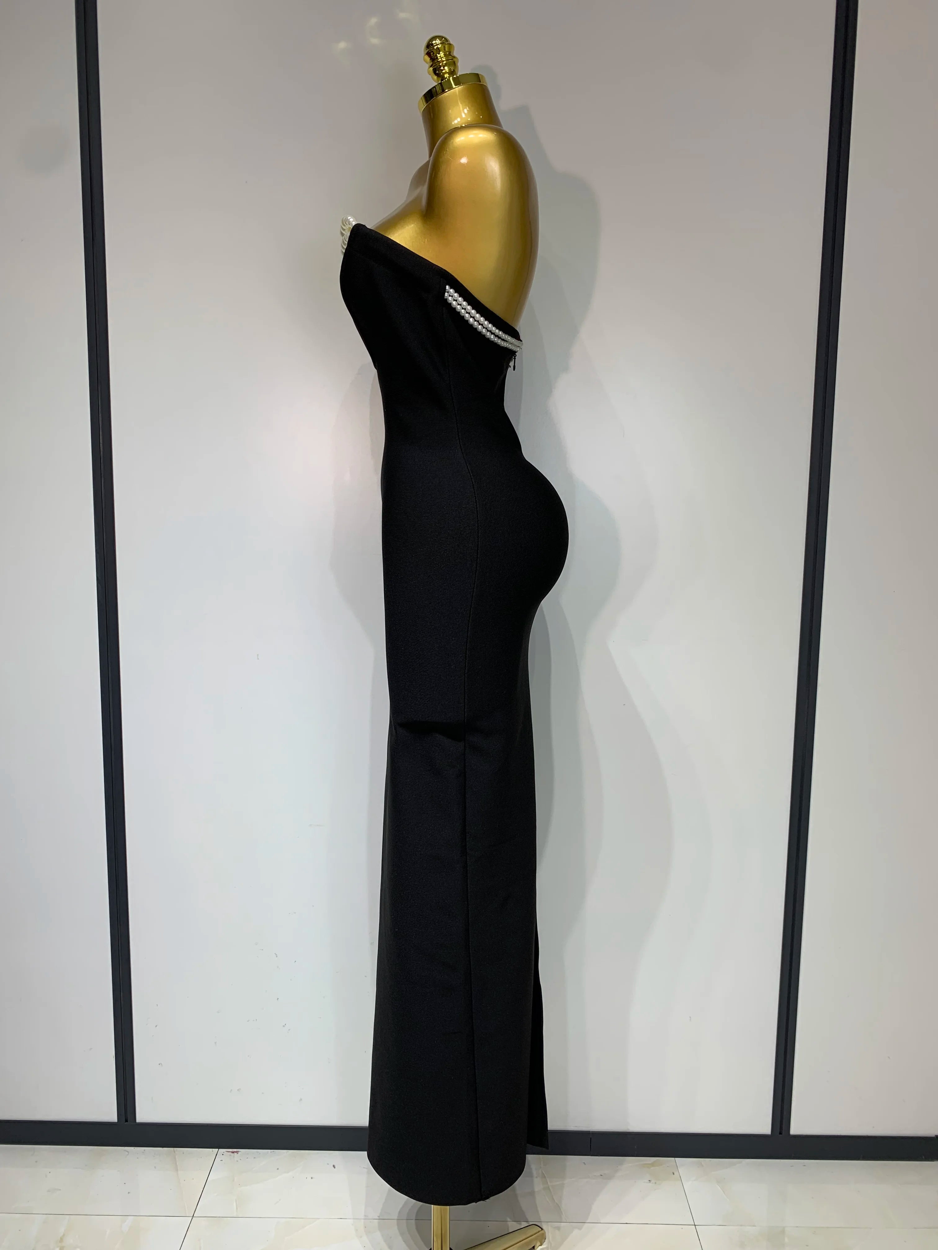 Black evening gown on a gold mannequin against a white wall with black vertical stripes.