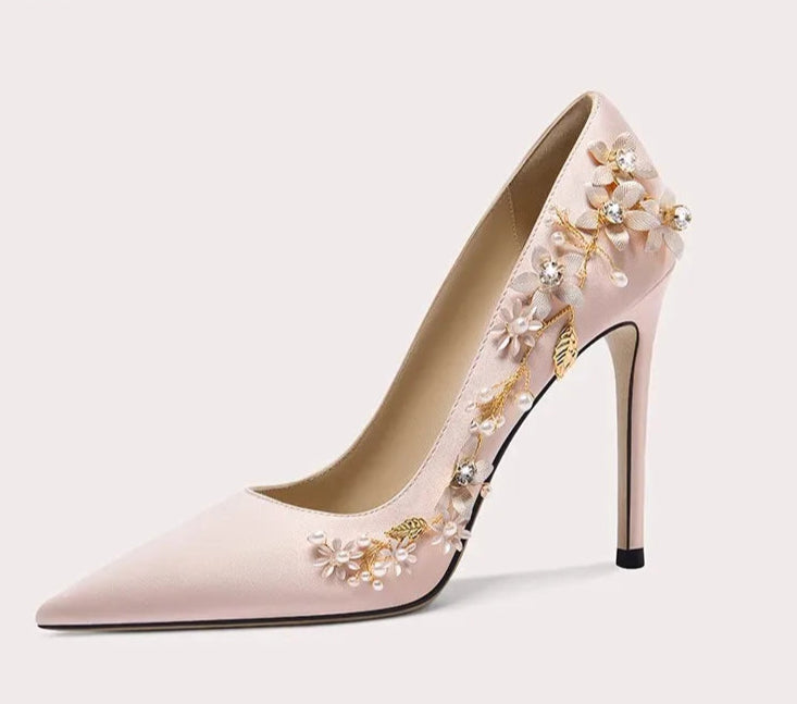 Pink high-heeled shoe with floral embellishments on a light gray background