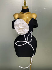 Black dress with a large white flower on a mannequin against a plain background