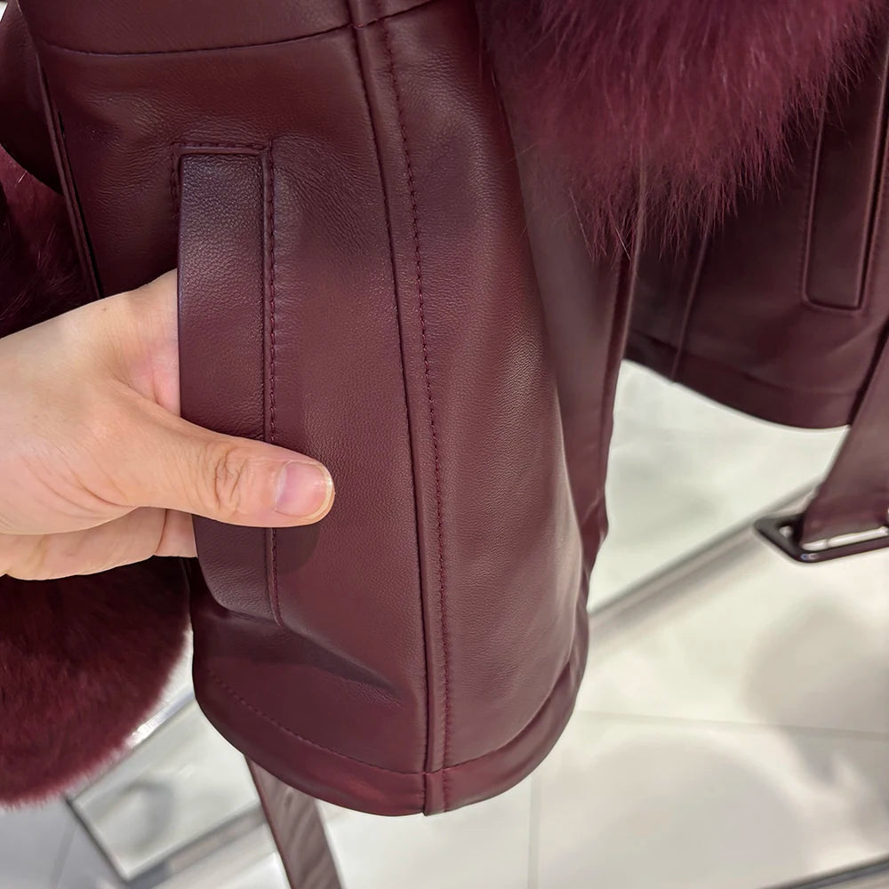Close-up of a maroon leather jacket with fur trim, held by a hand.