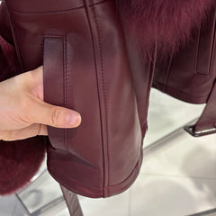 Close-up of a maroon leather jacket with fur trim, held by a hand.