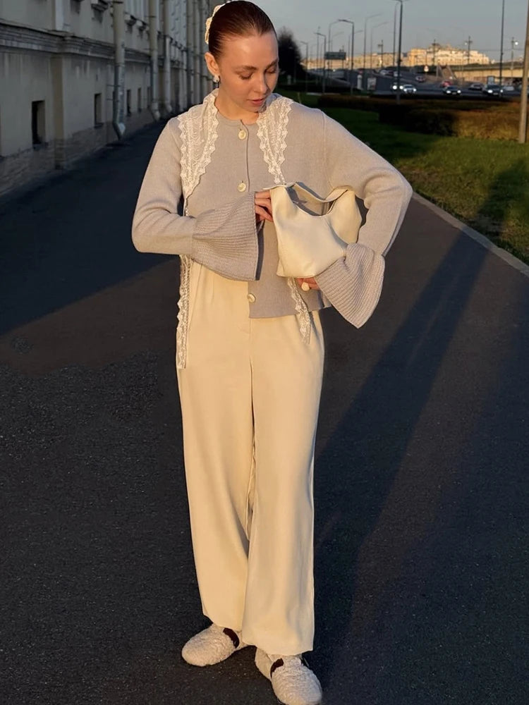 Woman in a light gray cardigan and beige pants standing on a street.