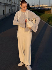 Woman in a light gray cardigan and beige pants standing on a street.