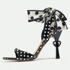 Black high-heeled shoe with white polka dots and a large bow on a white background