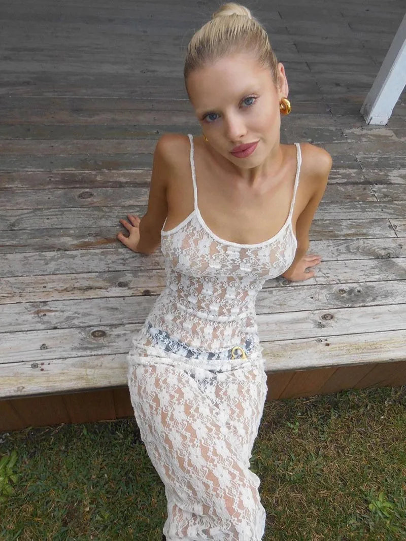Woman in a white lace dress sitting on a wooden bench outdoors.