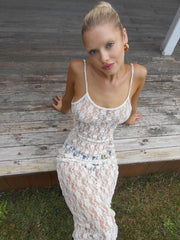 Woman in a white lace dress sitting on a wooden bench outdoors.