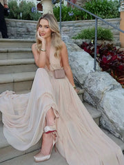 Woman in a flowing beige dress sitting on stone steps outdoors.