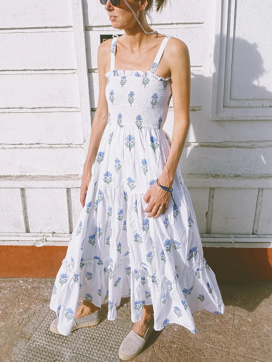 Woman wearing a white floral dress standing against a light-colored wall.