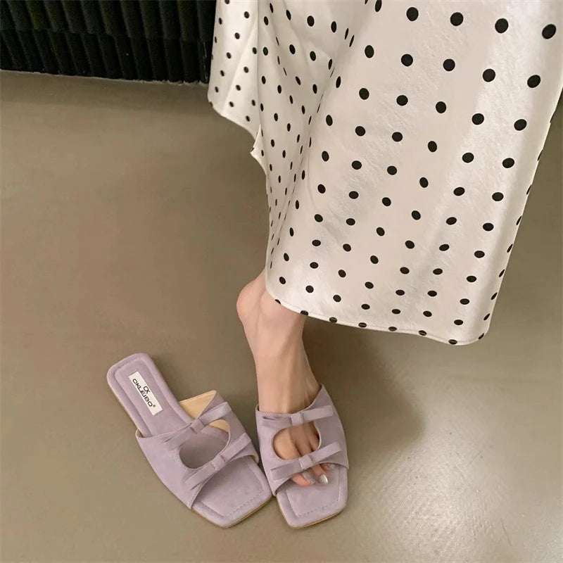 Purple slippers worn with a polka dot skirt on a neutral floor.