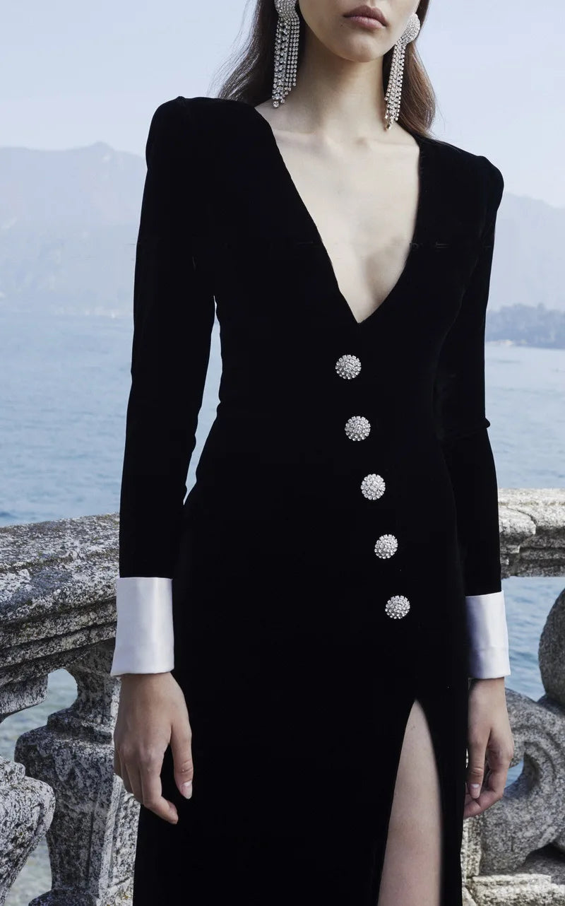 Black dress with silver buttons and a high slit worn by a model against a scenic background.