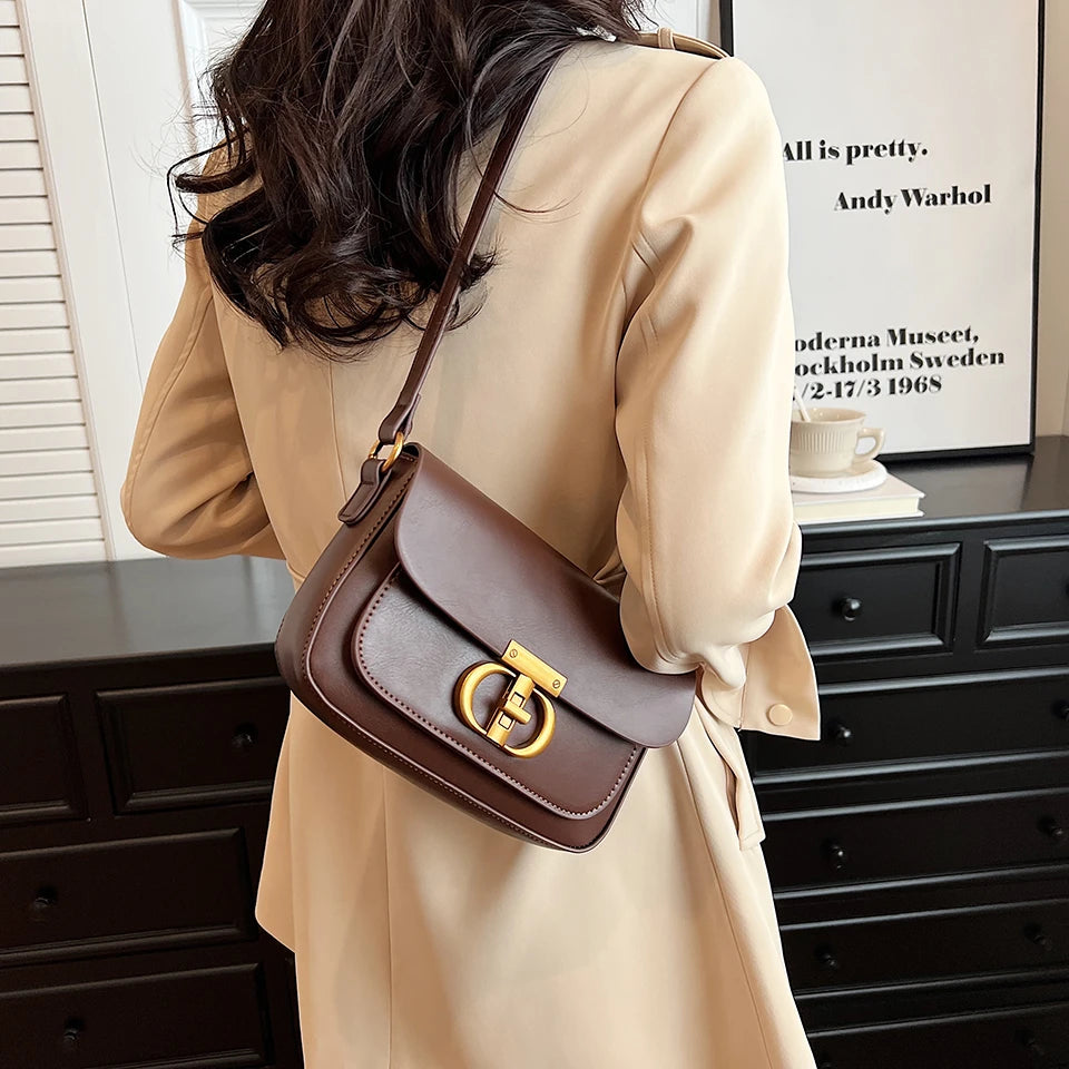 Person wearing a beige coat with a brown handbag featuring a gold clasp.