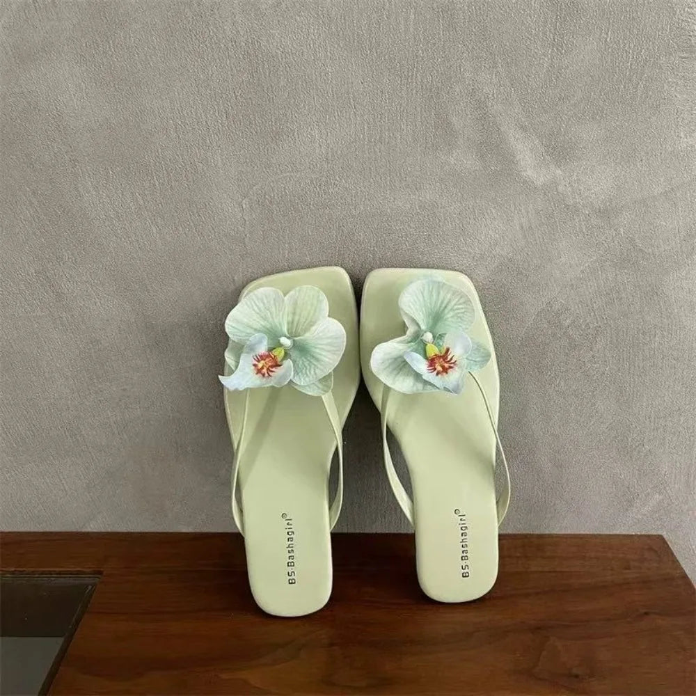 Pair of light green flip-flops with floral decorations on a wooden surface and gray background
