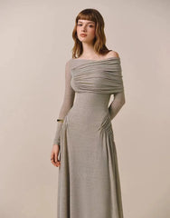 Woman wearing a long, off-shoulder gray dress against a plain background