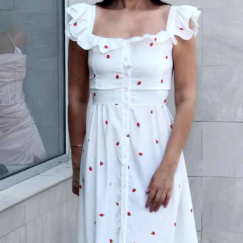 Woman wearing a white dress with red patterns against a light gray wall.