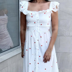 Woman wearing a white dress with red patterns against a light gray wall.