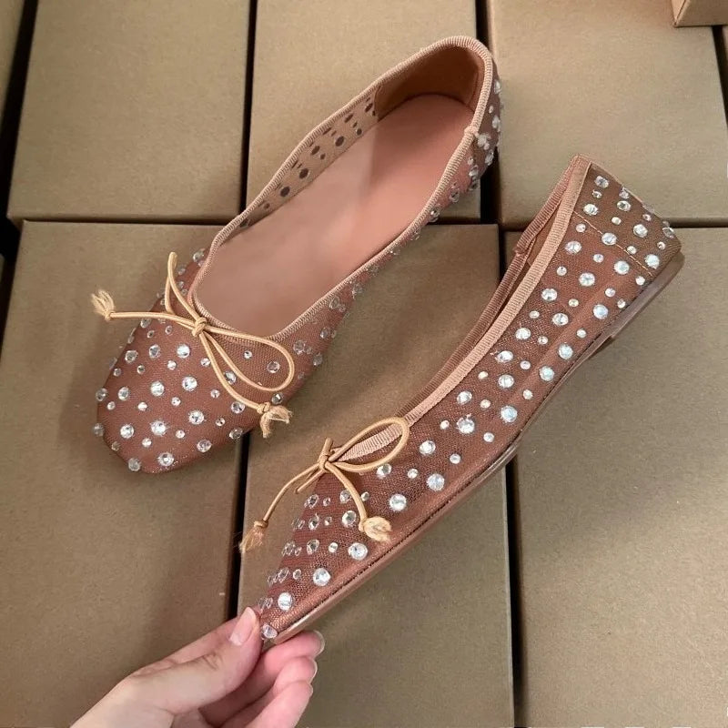 Close-up of a hand holding a beige mesh ballet flat with crystal embellishments.