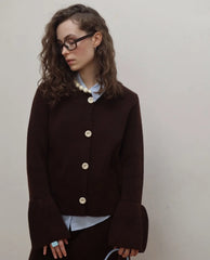 Woman wearing a dark brown jacket with white buttons against a plain background