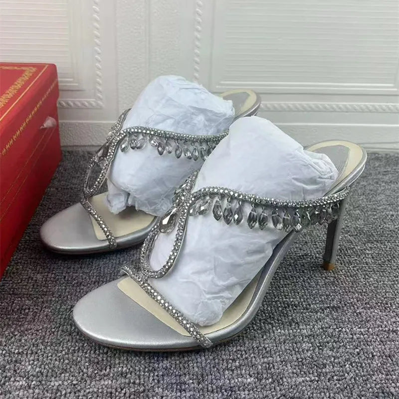 Silver high-heeled sandals with decorative straps on a carpeted floor.