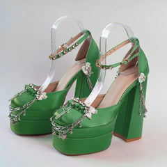 Green high-heeled shoes with clear straps and decorative elements on a light gray background