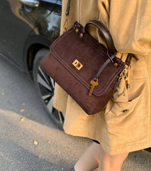 Brown handbag held by a person wearing a beige coat, with a car in the background.