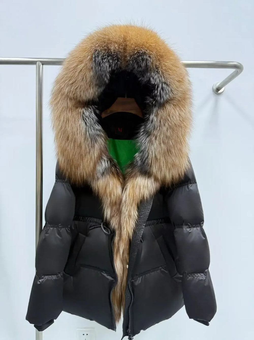 Black puffer jacket with a fur-lined hood on a rack against a light blue background