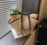 Woven straw bag with black handles on a surface near a window