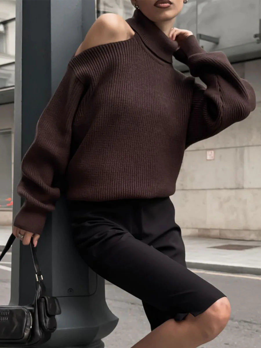 Person wearing a brown off-shoulder sweater and black pants, standing on a city street.