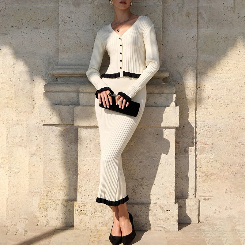 Woman in a white ribbed dress with black trim standing against a stone wall.