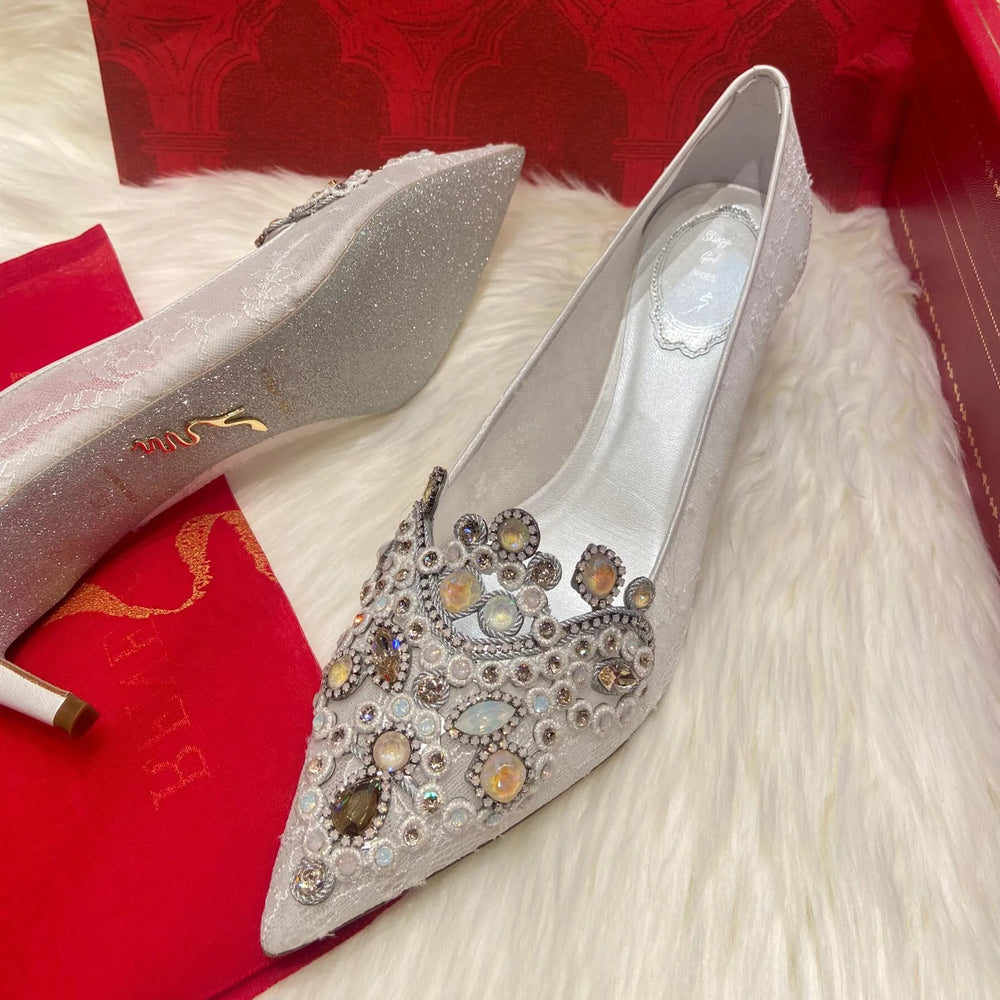 Silver high-heeled shoes with gemstone embellishments on a red fabric background