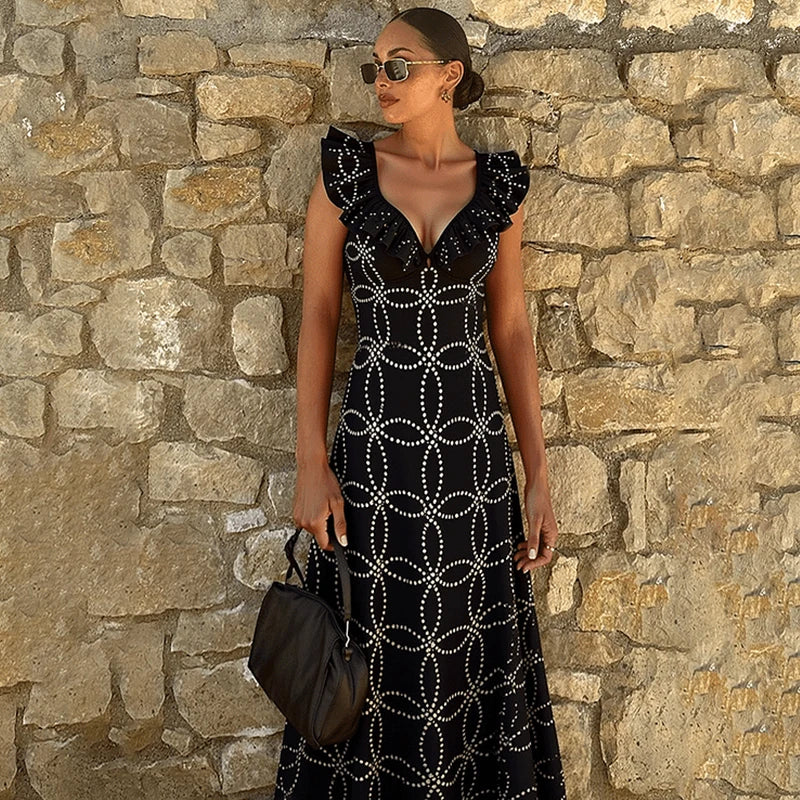 Black geometric print one-piece swimsuit with ruffles standing against a stone wall.