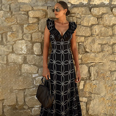 Black geometric print one-piece swimsuit with ruffles standing against a stone wall.