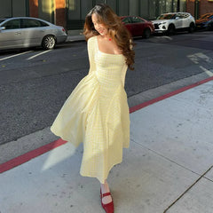 Woman in a light yellow dress standing on a city street.