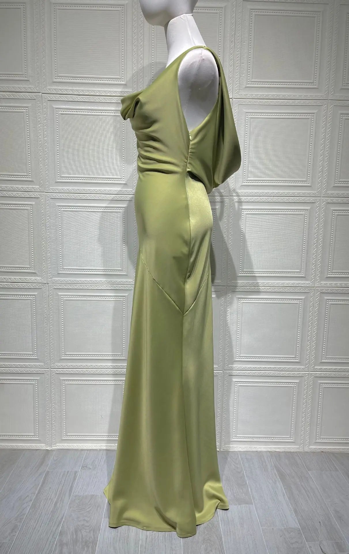 Mannequin wearing a light green evening gown against a white paneled wall.