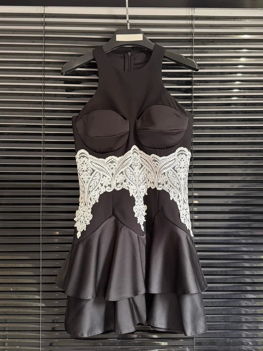 Black dress with white lace details on a hanger against a metallic background