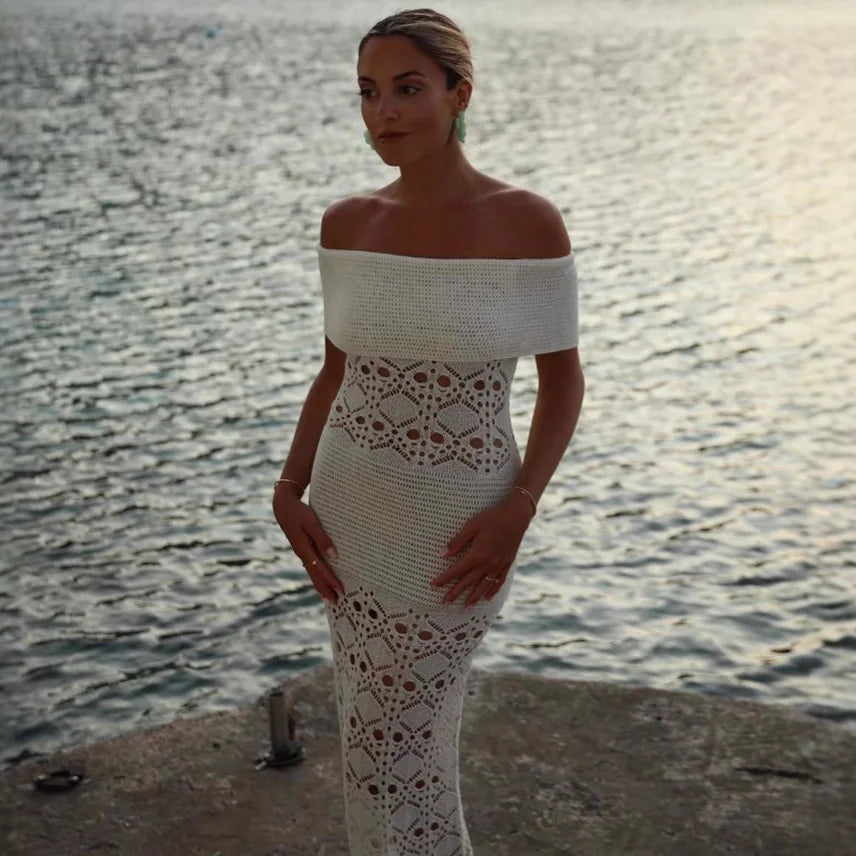 Woman in a white crochet dress standing by a body of water.