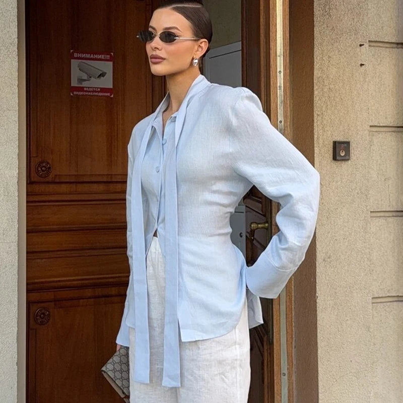 Woman wearing a light blue shirt and white pants standing in front of a building entrance.