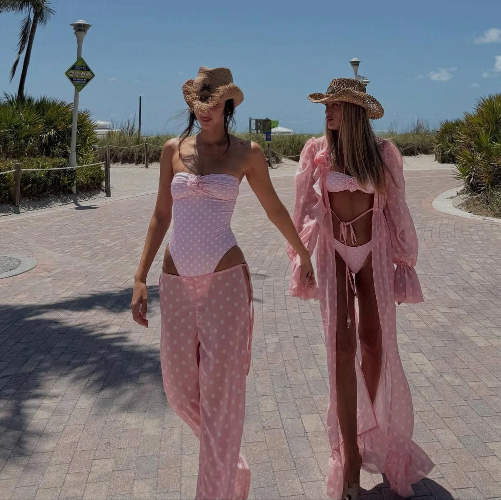 Two individuals walking on a boardwalk wearing pink polka dot swimwear and cover-ups.