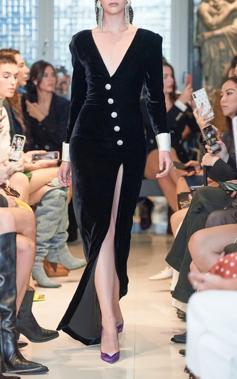 Model wearing a black velvet dress with a high slit on a runway.