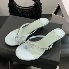 Light green high-heeled sandals with rhinestone straps on a black surface.